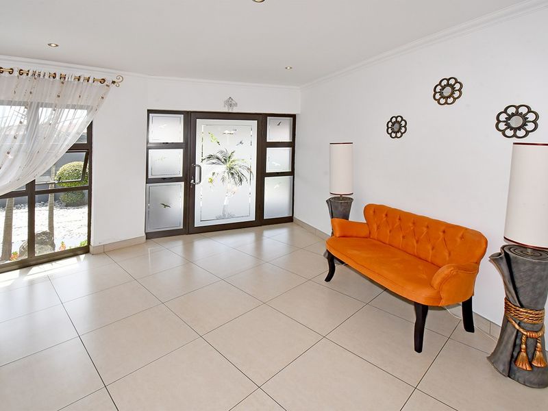 A bright and spacious entrance hall featuring large format floor tiles, recessed lighting, and a decorative frosted glass front door.