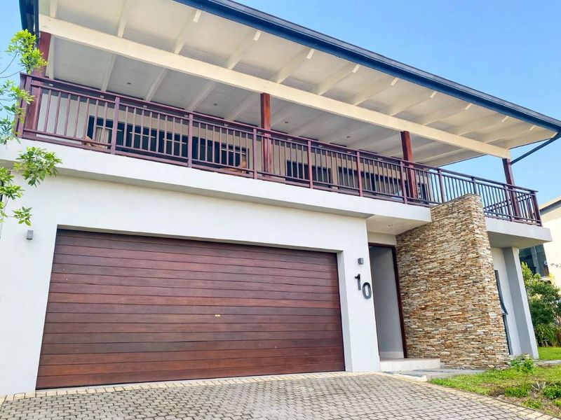 Modern two-story residential facade featuring a timber sectional garage door, stone feature wall, and a spacious covered upper-level balcony with timber railings.