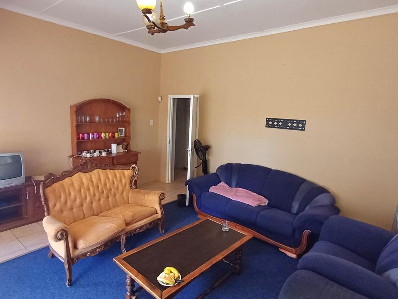 A spacious living room featuring neutral wall tones, blue carpeting, and a central ceiling light fixture.
