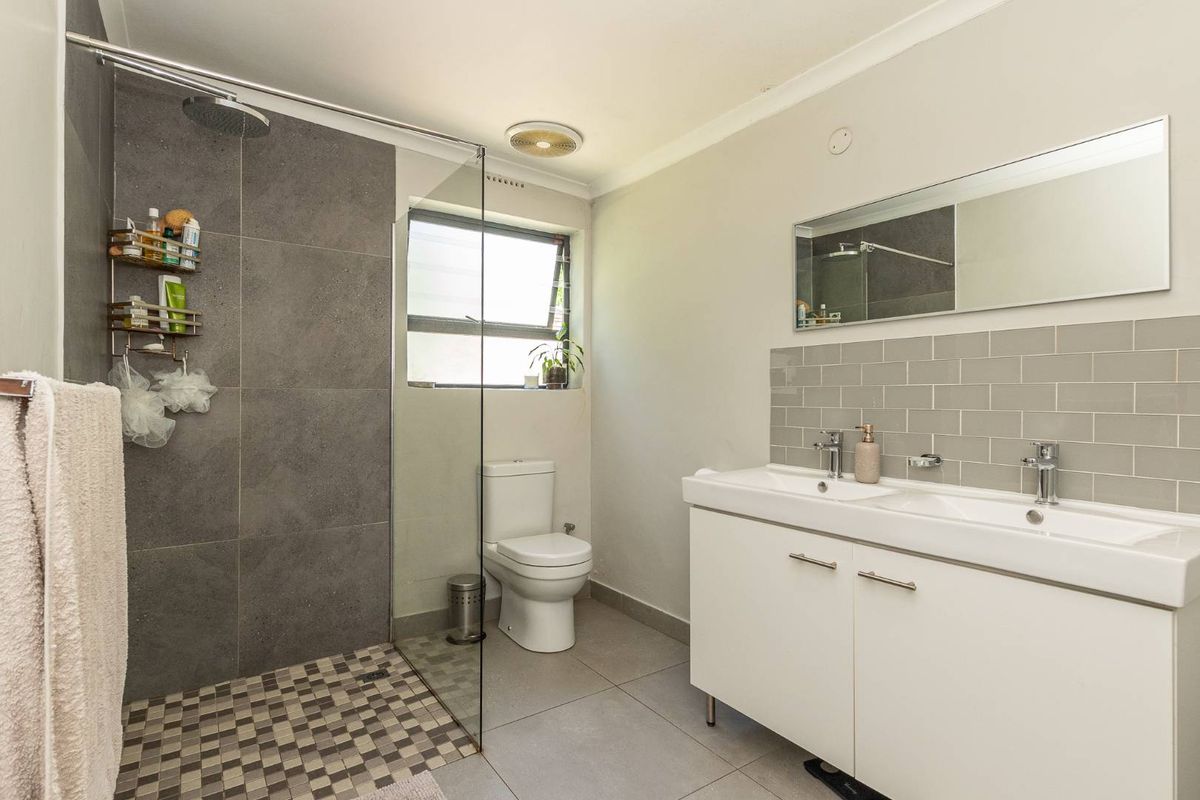 Modern bathroom featuring a walk-in shower with grey tiling, a double vanity with white cabinetry, and a wall-mounted mirror.