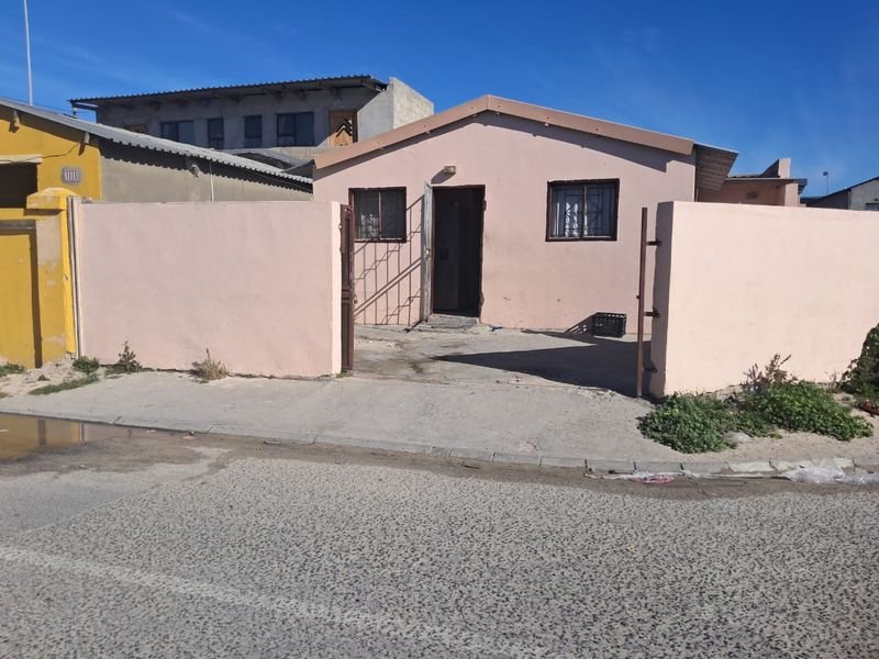 Front view of a single-story house featuring a perimeter wall, gated entrance, and concrete driveway area.