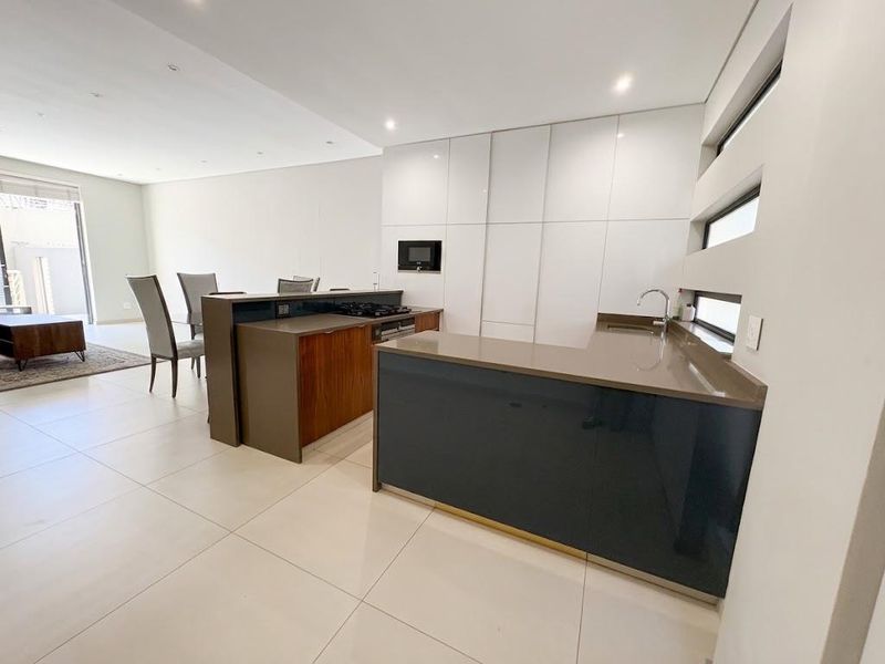 Modern open-plan kitchen featuring sleek high-gloss cabinetry, stone countertops, integrated appliances, and a breakfast bar, seamlessly flowing into the living area.