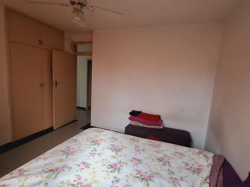A bedroom featuring built-in cupboards, a ceiling fan, and tiled flooring, requiring some cosmetic updates to the walls and ceiling.