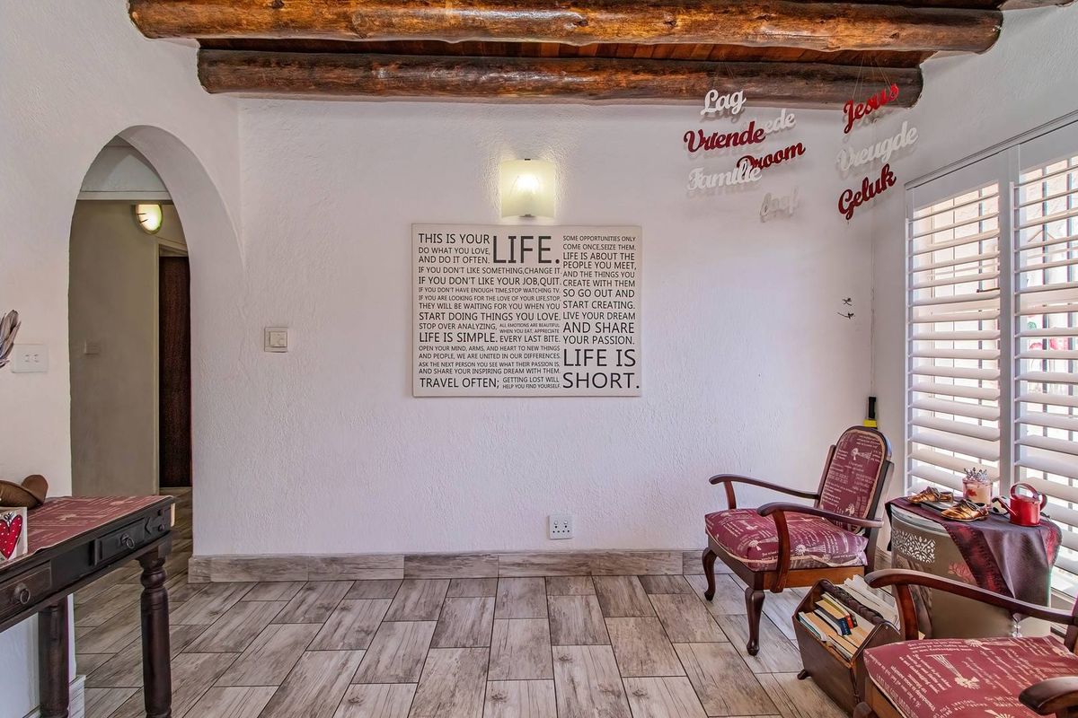 A cozy living area featuring rustic exposed timber ceiling beams, tiled flooring, and an arched entryway, complemented by natural light through shutter blinds.