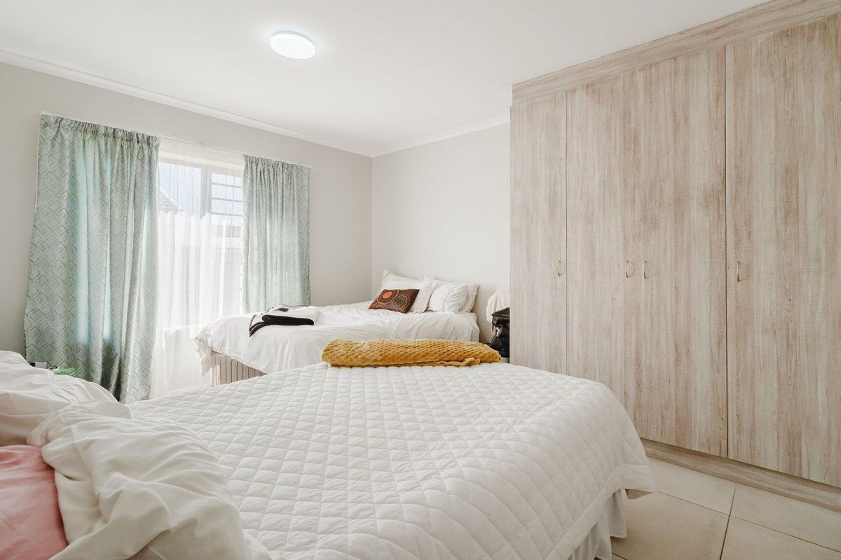 A well-lit bedroom featuring neutral walls, tiled flooring, and ample built-in cupboard storage space.