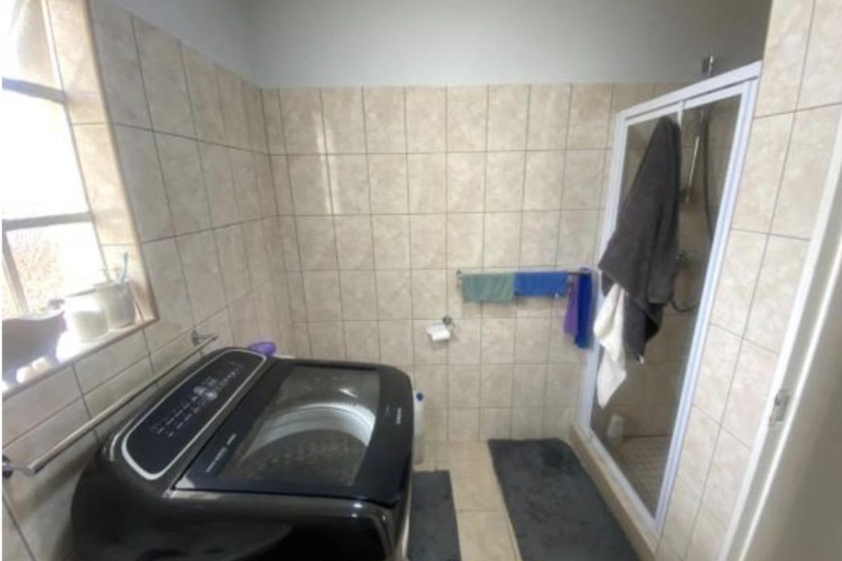 A functional bathroom featuring tiled walls, a glass-enclosed shower, and space for laundry appliances.