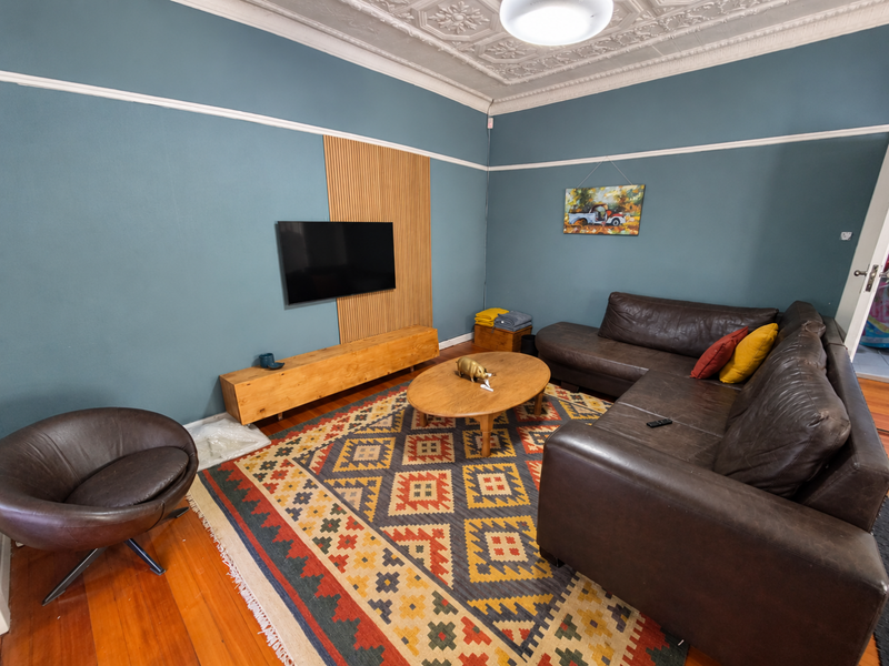 A cozy living room featuring original pressed metal ceilings, decorative ceiling roses, timber flooring, and a modern slat wall feature.