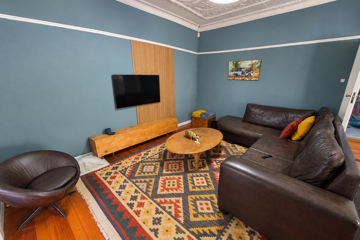 A cozy living room featuring original pressed metal ceilings, decorative ceiling roses, timber flooring, and a modern slat wall feature.