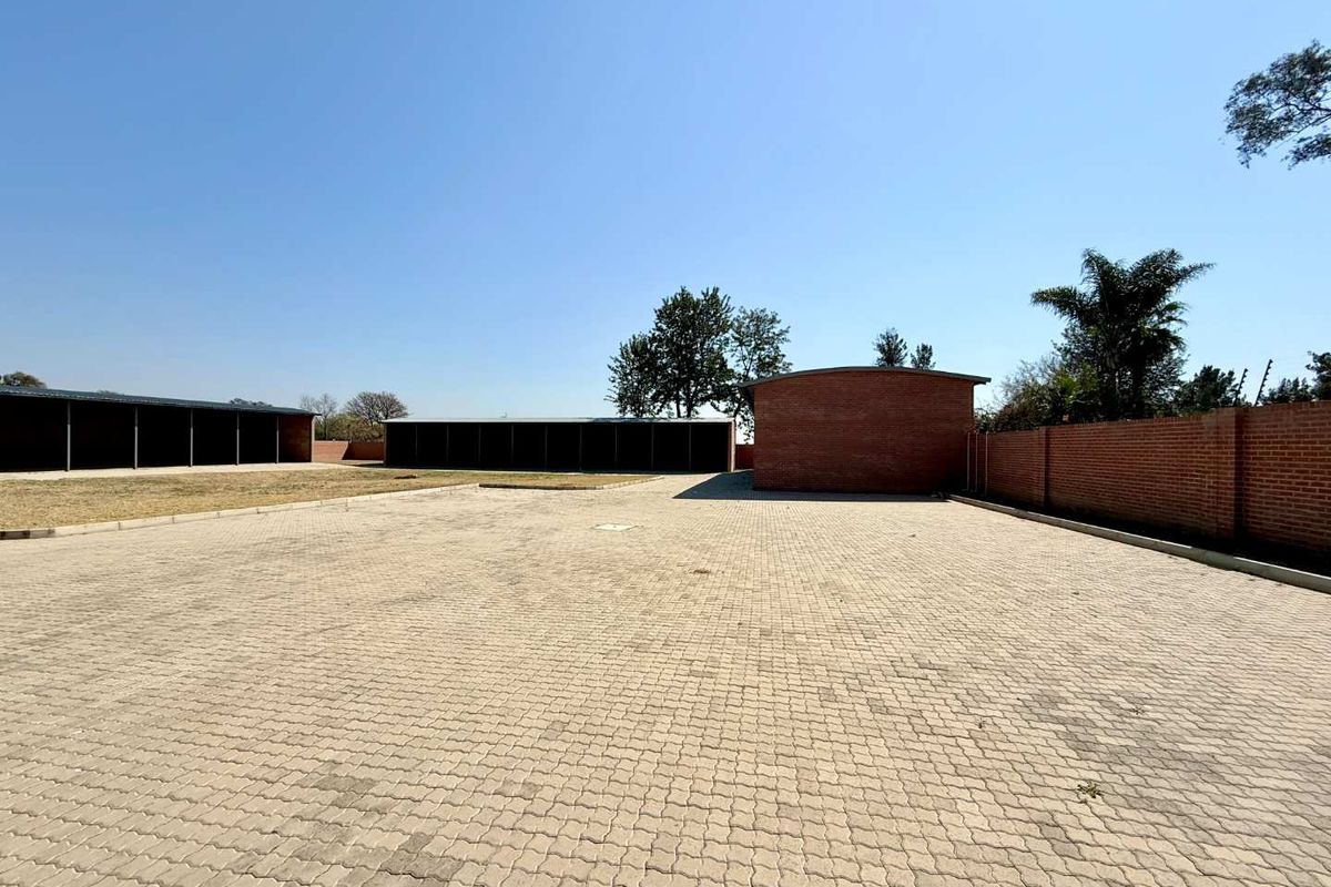 Expansive paved courtyard area featuring multiple covered storage or utility structures and perimeter brick boundary walls on a farm property.