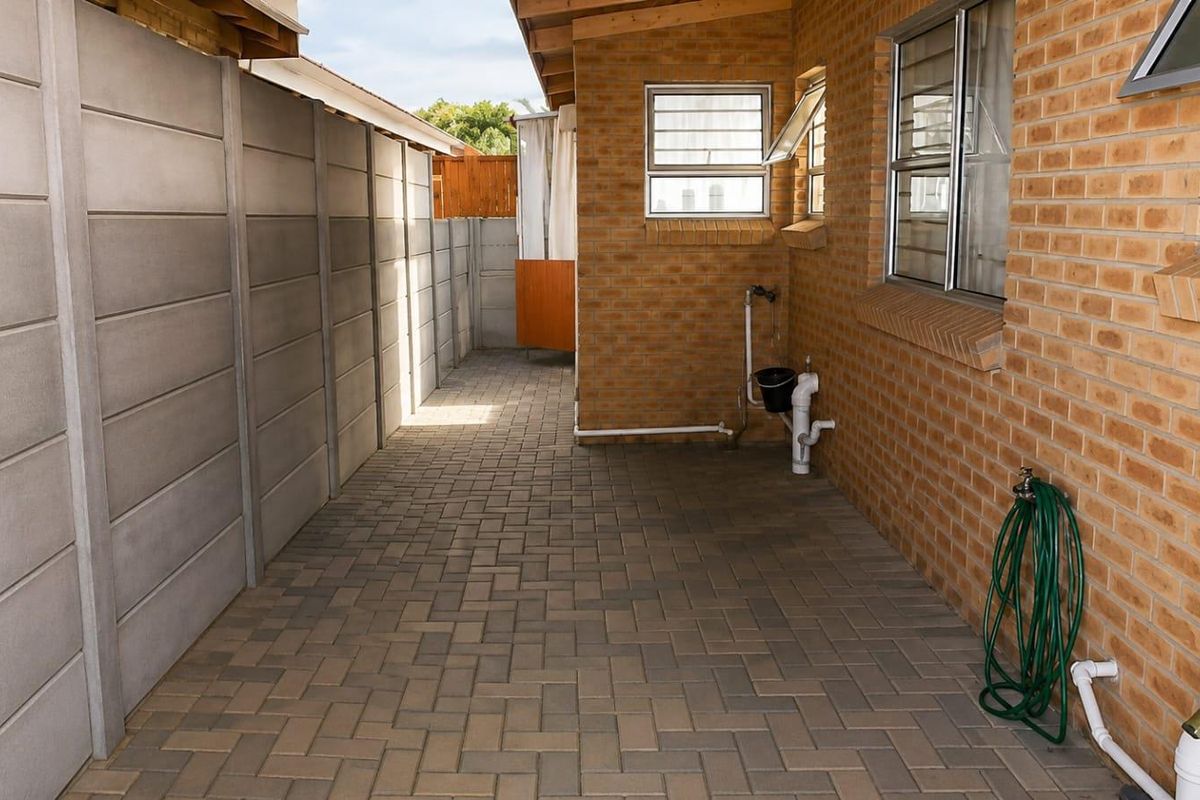 A paved rear courtyard area featuring brick exterior walls, precast concrete boundary fencing, and external plumbing fixtures.