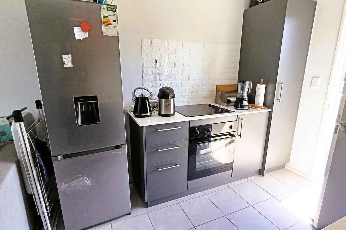 Compact kitchen area featuring modern grey cabinetry, a built-in oven, electric hob, and tiled flooring.