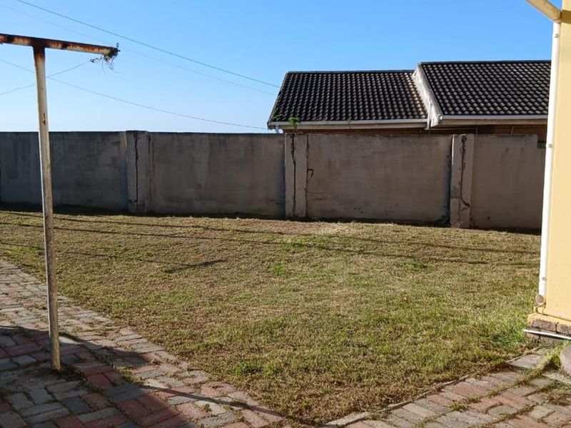 A rear garden area featuring a paved patio, lawn, and a precast concrete boundary wall.