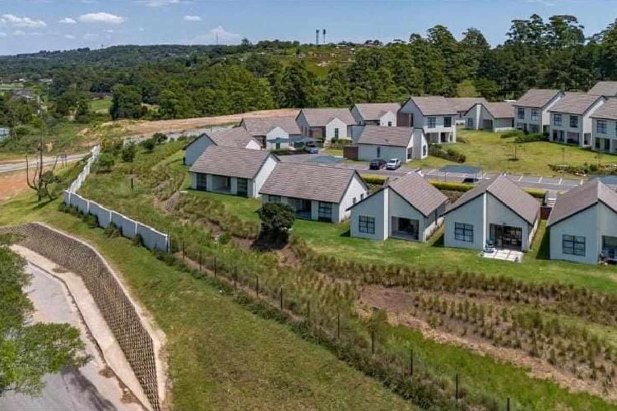 Aerial view of a modern townhouse complex featuring multiple residential units, landscaped green spaces, and paved access roads within a secure estate setting.
