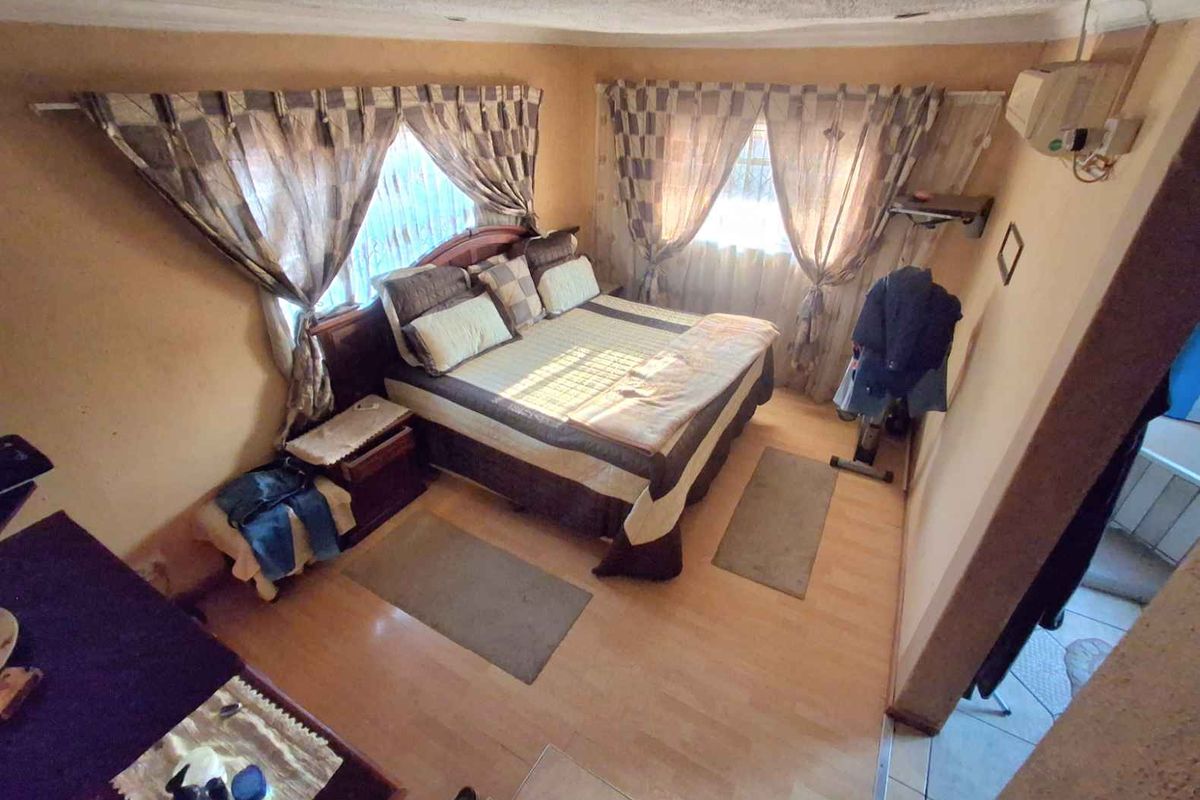 A bedroom featuring laminate flooring, dual windows with curtains, and a wall-mounted air conditioning unit.