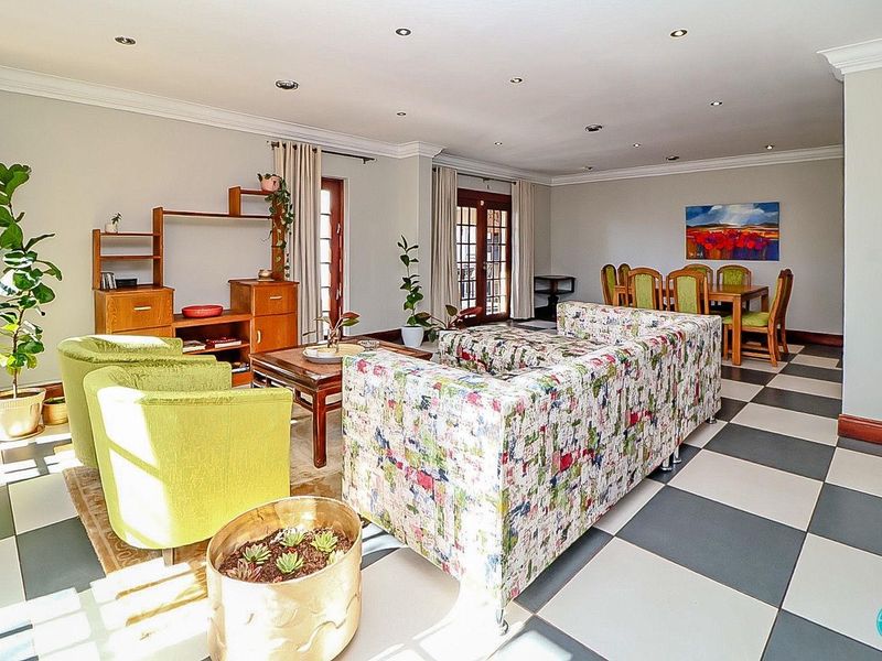 Spacious open-plan living and dining area featuring large format checkered floor tiles, recessed lighting, and double french doors leading to the exterior.