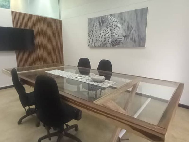 A professional office meeting room featuring a modern glass-topped table, slatted wood accent wall, and a transom window for natural light.