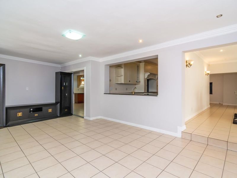 Open plan living area featuring tiled flooring, crown molding, and a service window connecting to the kitchen, with an adjacent raised dining space.