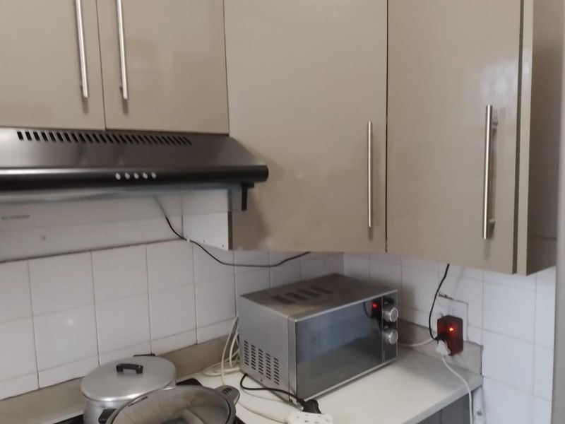 A compact kitchen area featuring built-in cabinetry, a tiled backsplash, and an extractor fan, requiring minor maintenance to address exposed wiring.