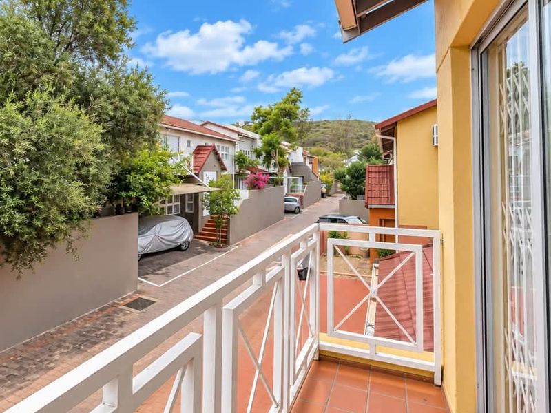 A clean, well-maintained balcony with tiled flooring and a white metal balustrade, offering an elevated view of the townhouse complex and street.