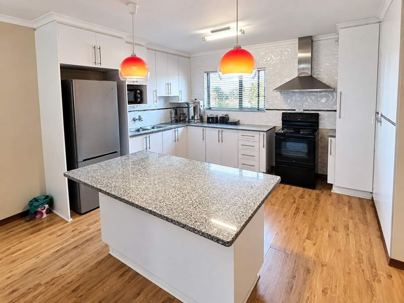 Modern kitchen featuring granite countertops, a central island, stainless steel extractor fan, and ample built-in cabinetry with a tiled backsplash.