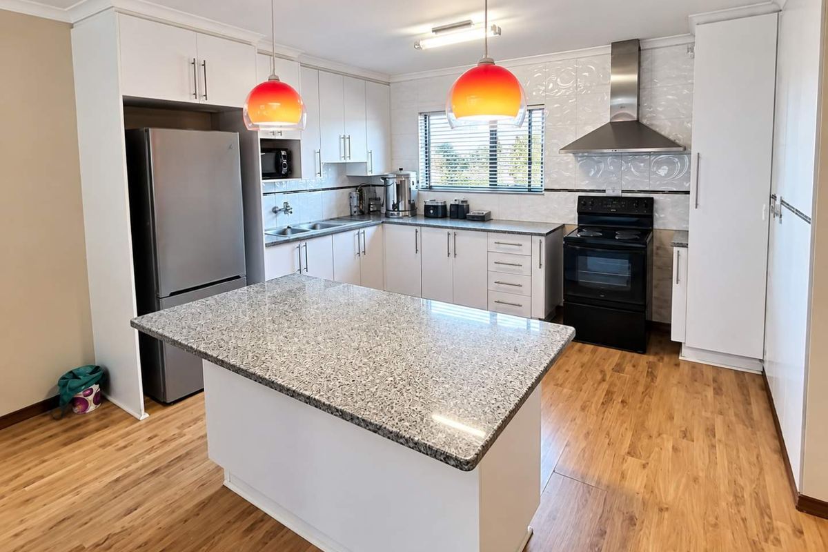 Modern kitchen featuring granite countertops, a central island, stainless steel extractor fan, and ample built-in cabinetry with a tiled backsplash.