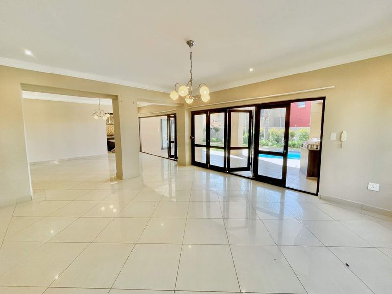 Spacious open-plan living area featuring polished porcelain tiles, modern chandelier lighting, and large stacking doors providing seamless access to the outdoor pool area.