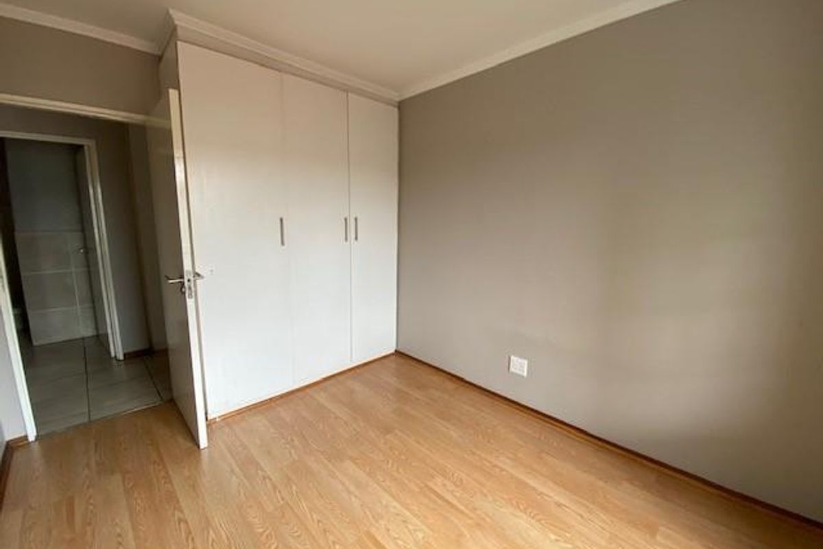 A clean, empty bedroom featuring light wood-look laminate flooring and built-in white cabinetry, with an adjacent view into a tiled bathroom area.