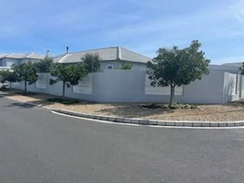 Street view of the property showing the perimeter wall, tiled roof, and surrounding landscaped trees.