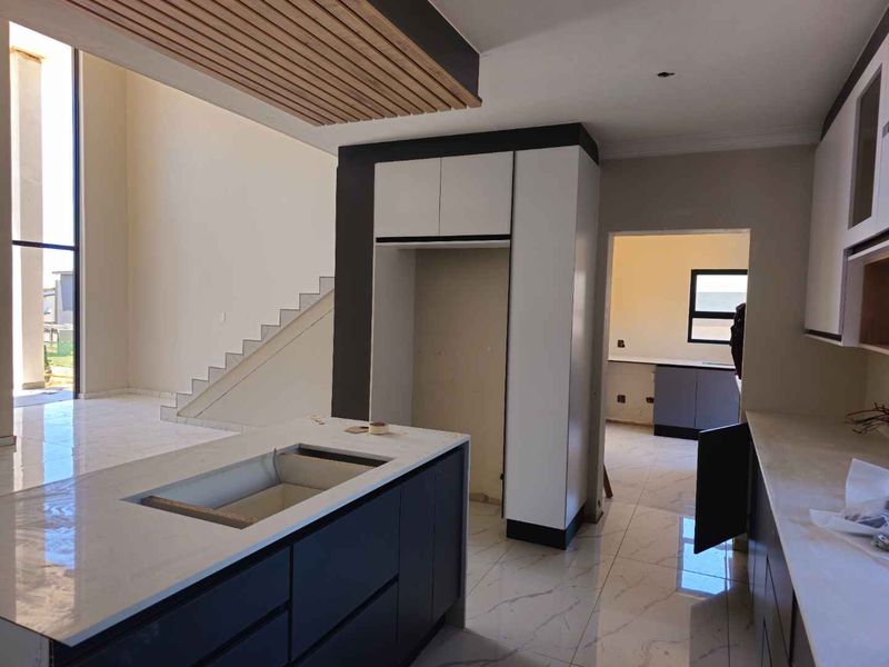 Modern open-plan kitchen area featuring a central island, stone countertops, and a distinctive slatted timber ceiling detail, currently in the final stages of completion.