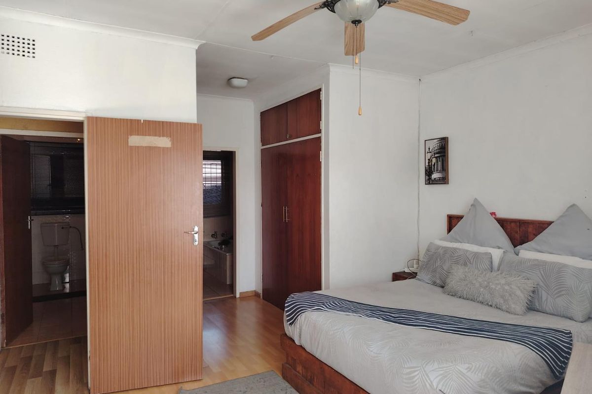 A bedroom featuring built-in wooden cupboards, a ceiling fan, and direct access to an en-suite bathroom with tiled flooring.