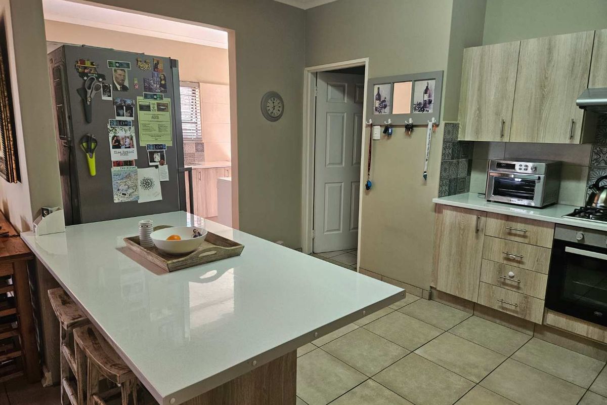 A functional kitchen featuring light wood cabinetry, a white stone-topped island, built-in oven, and tiled flooring, with an adjacent scullery area visible.