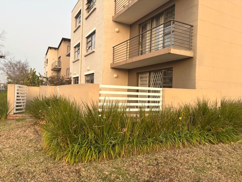 Exterior view of an apartment building featuring a ground floor patio with a boundary wall and upper-level balconies with metal railings.