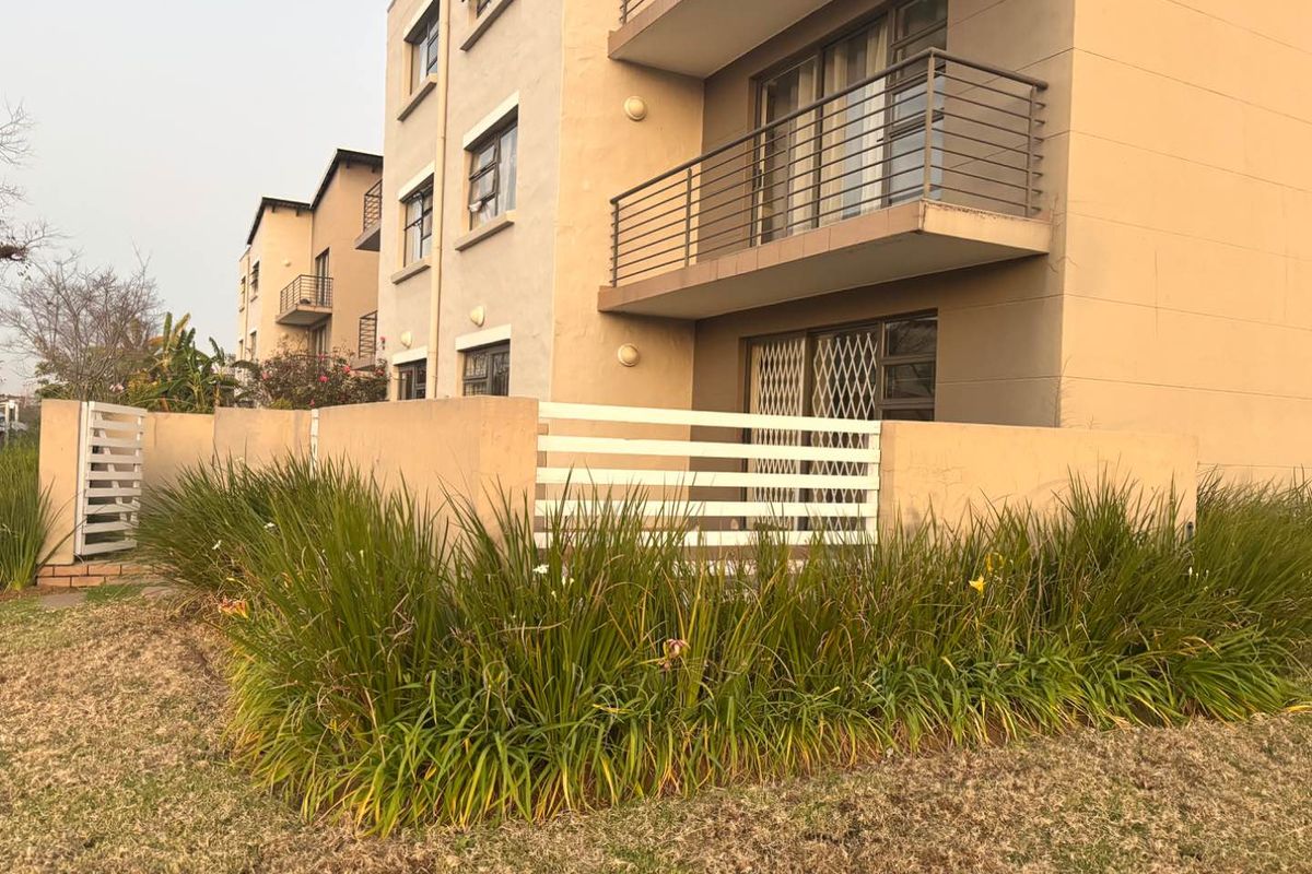 Exterior view of an apartment building featuring a ground floor patio with a boundary wall and upper-level balconies with metal railings.