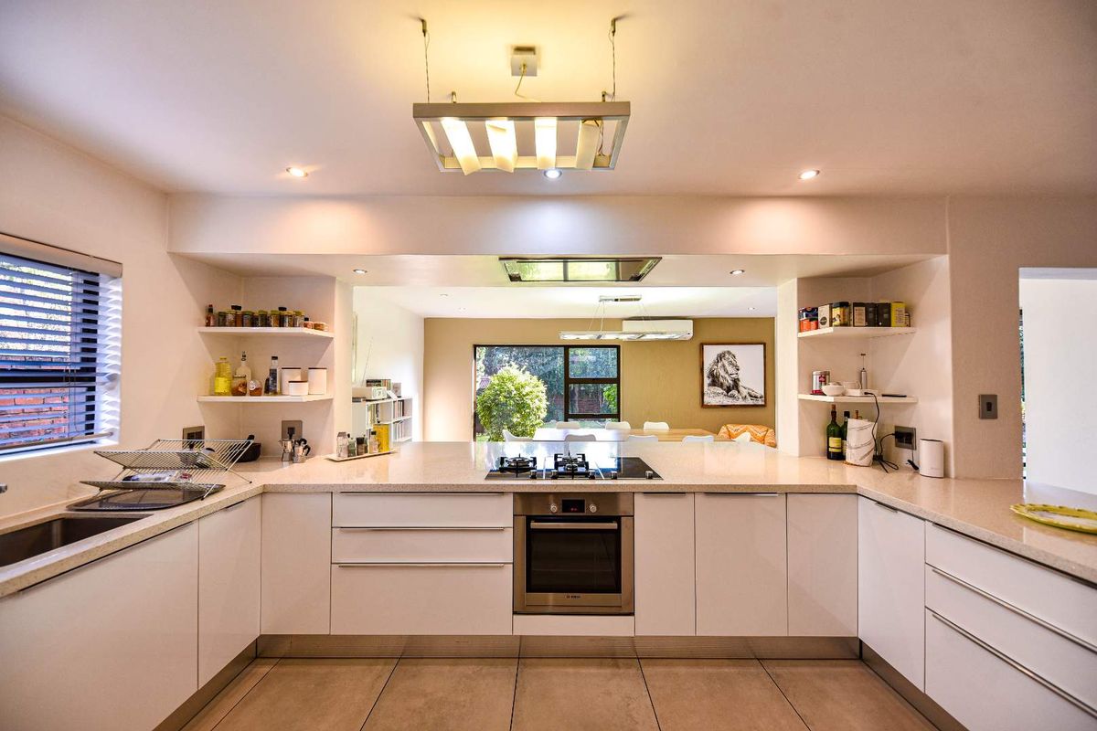 Modern open-plan kitchen featuring sleek white cabinetry, stone countertops, integrated oven and hob, and recessed lighting, flowing into the adjacent dining area.