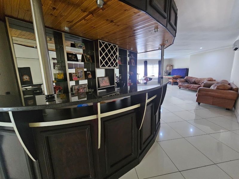 A spacious entertainment area featuring a large built-in bar with timber ceiling detailing, mirrored shelving, and integrated wine storage, flowing into the living space.
