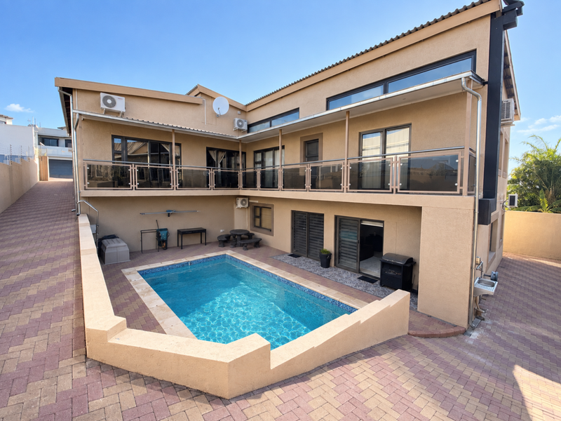 Rear exterior view featuring a swimming pool, paved patio area, and a spacious upper-level balcony with glass balustrades.