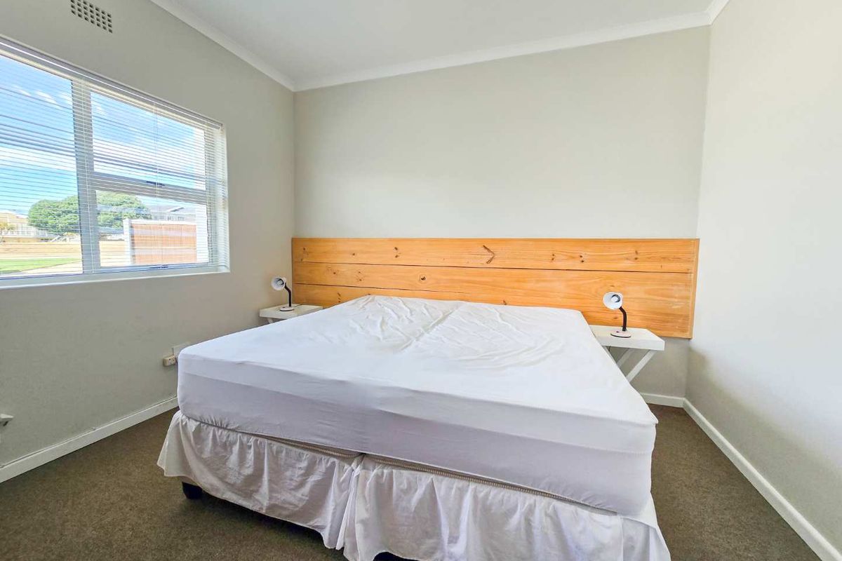 A bright bedroom featuring neutral wall tones, carpeted flooring, and a built-in timber headboard feature wall.