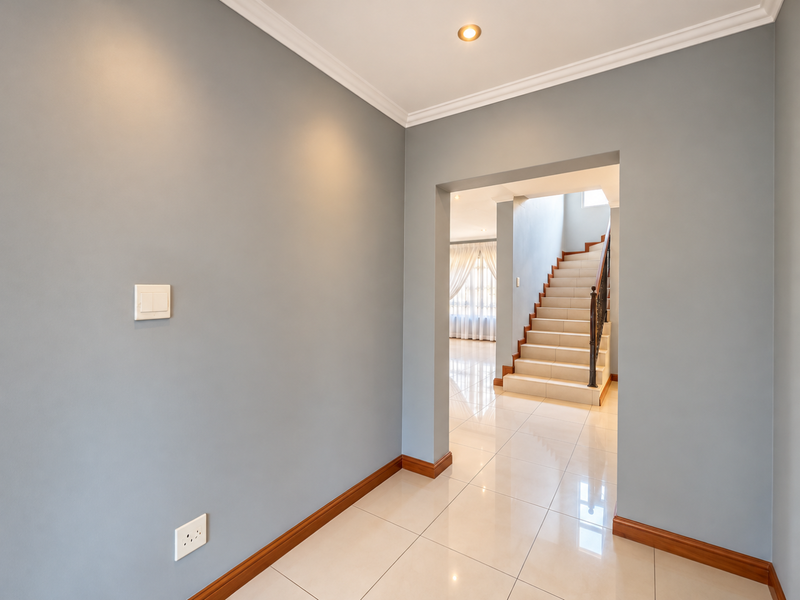 A bright, modern hallway featuring polished tile flooring, neutral grey walls, and a staircase with a wrought iron balustrade leading to the upper level.