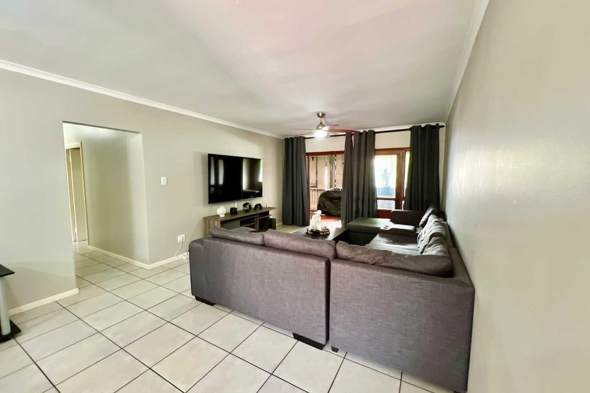 A spacious living room featuring neutral wall tones, tiled flooring, and a ceiling fan, with direct access to an outdoor patio area.
