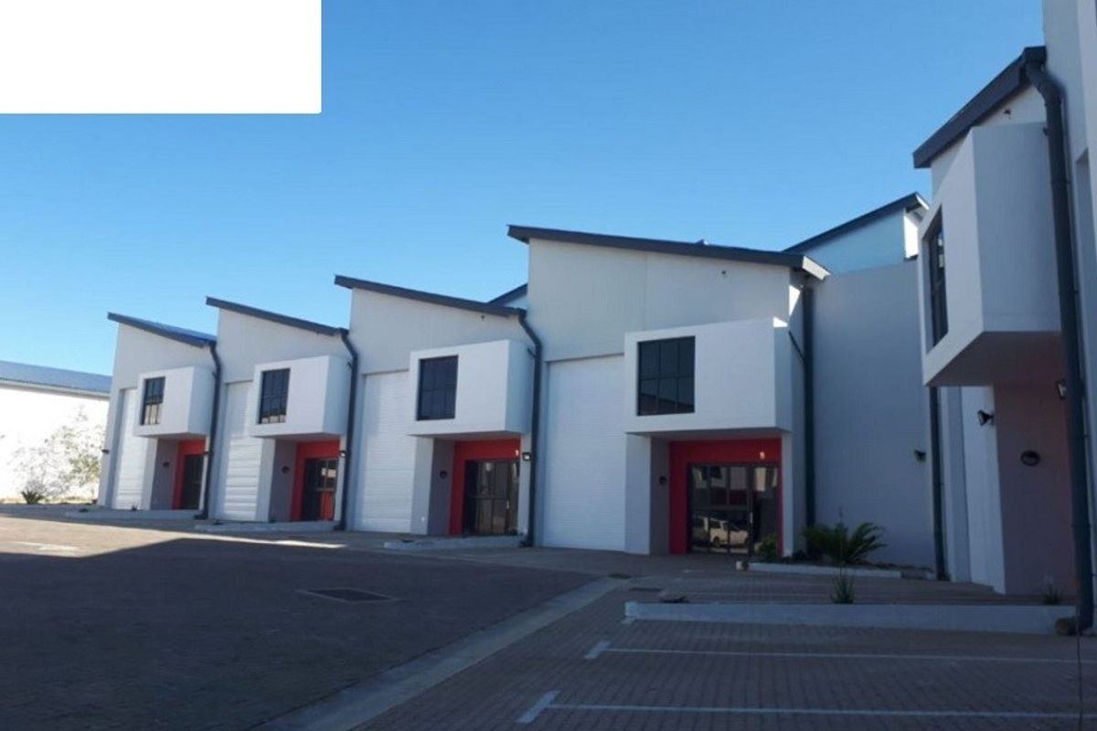 Modern industrial complex featuring multiple units with roller shutter doors, paved parking, and clean architectural lines.