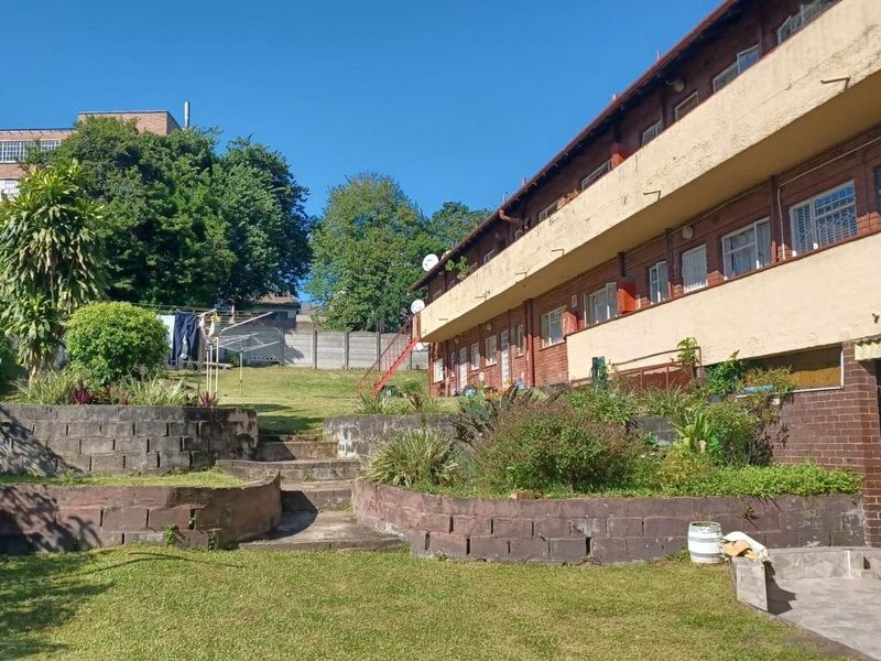 Rear view of the apartment building featuring a terraced garden with concrete retaining walls, stairs, and access to the building's balcony level.