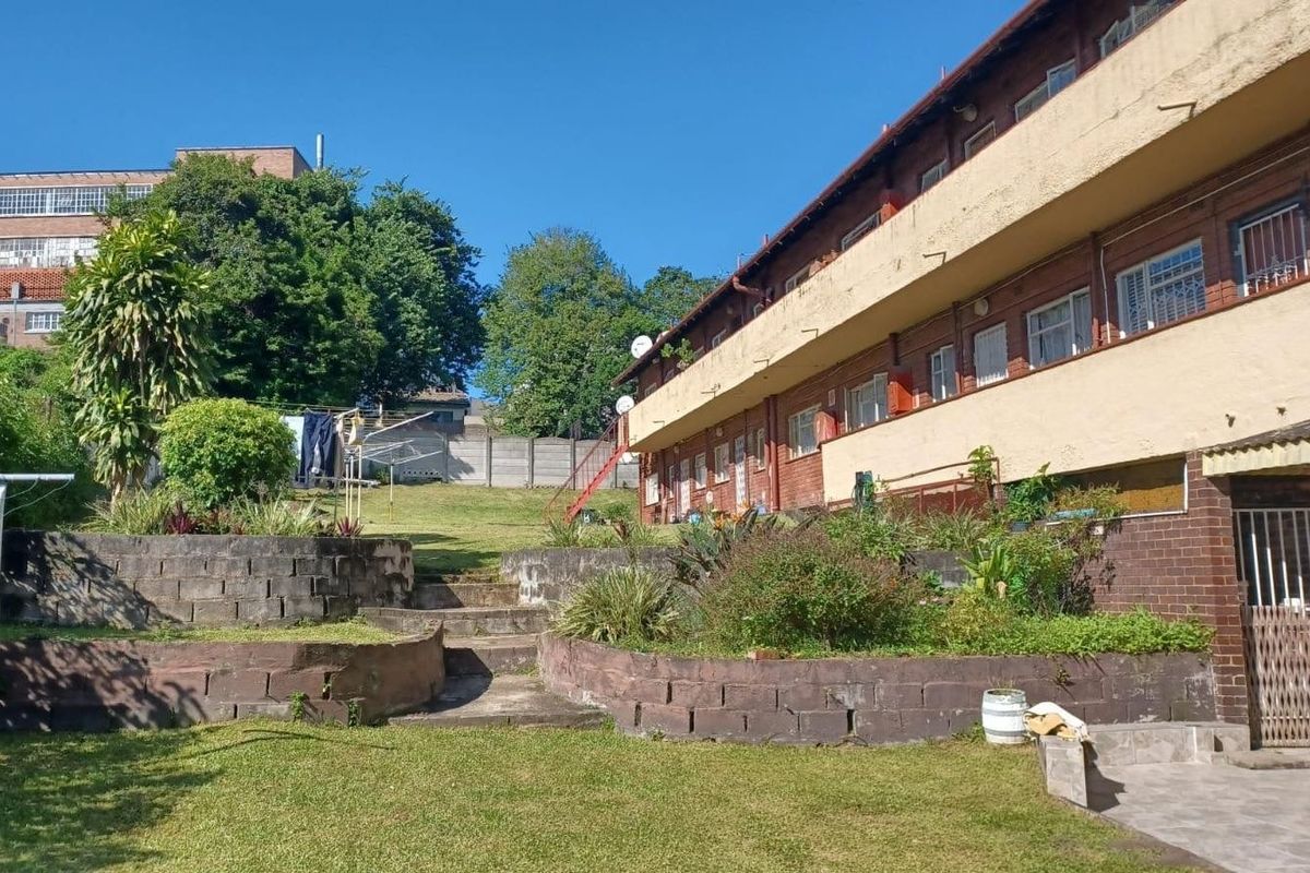 Rear view of the apartment building featuring a terraced garden with concrete retaining walls, stairs, and access to the building's balcony level.