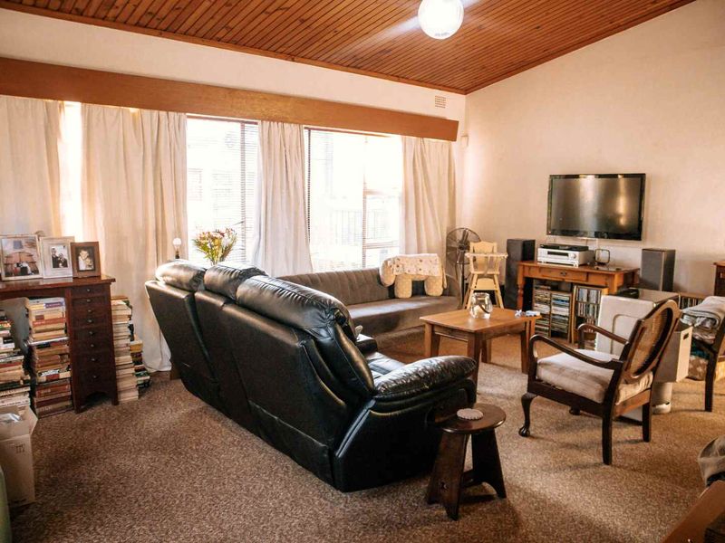 A spacious living room featuring a distinctive timber-clad ceiling, large windows allowing natural light, and carpeted flooring throughout.