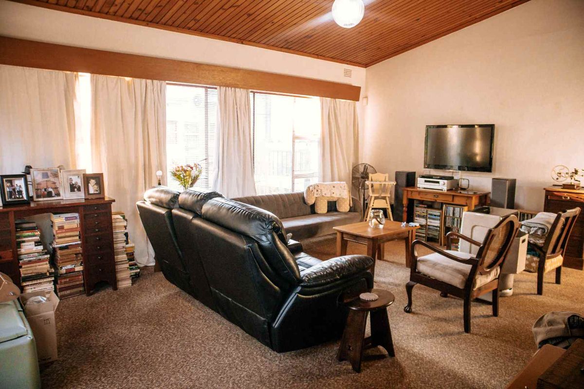 A spacious living room featuring a distinctive timber-clad ceiling, large windows allowing natural light, and carpeted flooring throughout.