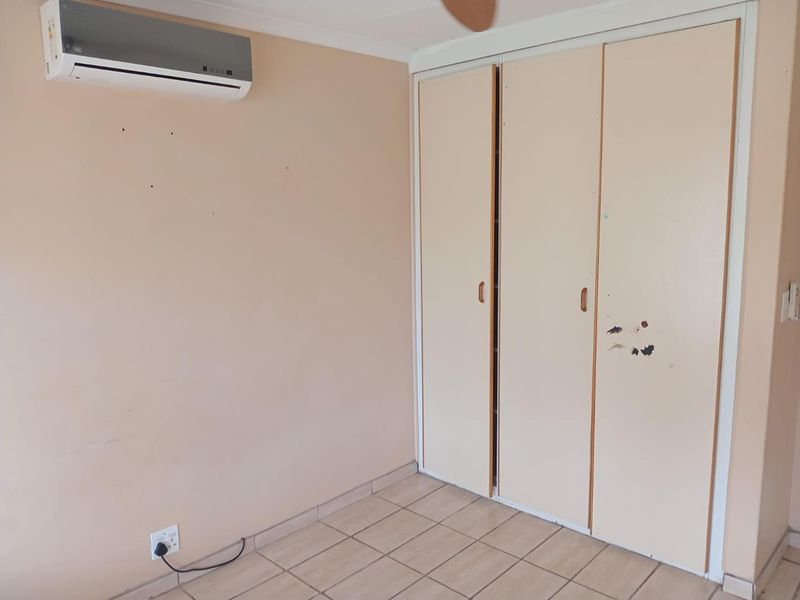 An empty bedroom featuring tiled flooring, a built-in wardrobe, and a wall-mounted split-system air conditioner.