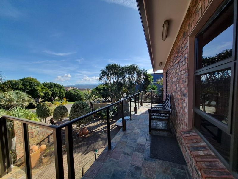 A spacious elevated balcony featuring durable tiled flooring, a modern glass and metal balustrade, and views over the landscaped garden and surrounding neighborhood.