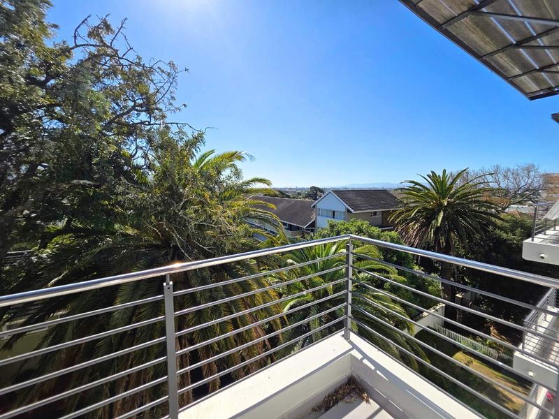 A sunny balcony featuring a modern stainless steel balustrade with elevated views over the surrounding neighborhood and mature trees.