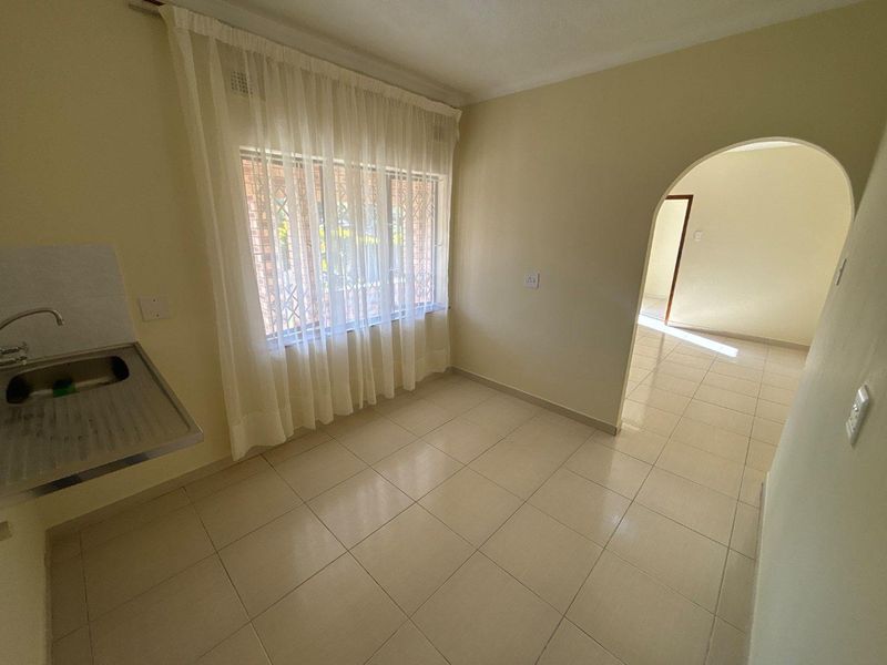 A compact, empty kitchen area featuring tiled flooring, a stainless steel sink, and an arched doorway leading to an adjacent room.