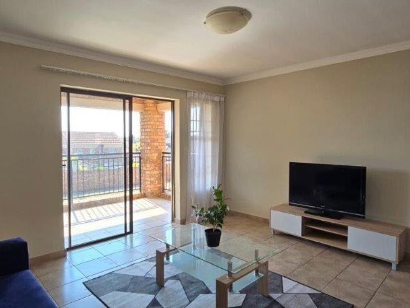 A living room featuring tiled flooring, neutral walls, and a sliding glass door providing access to an outdoor balcony area.
