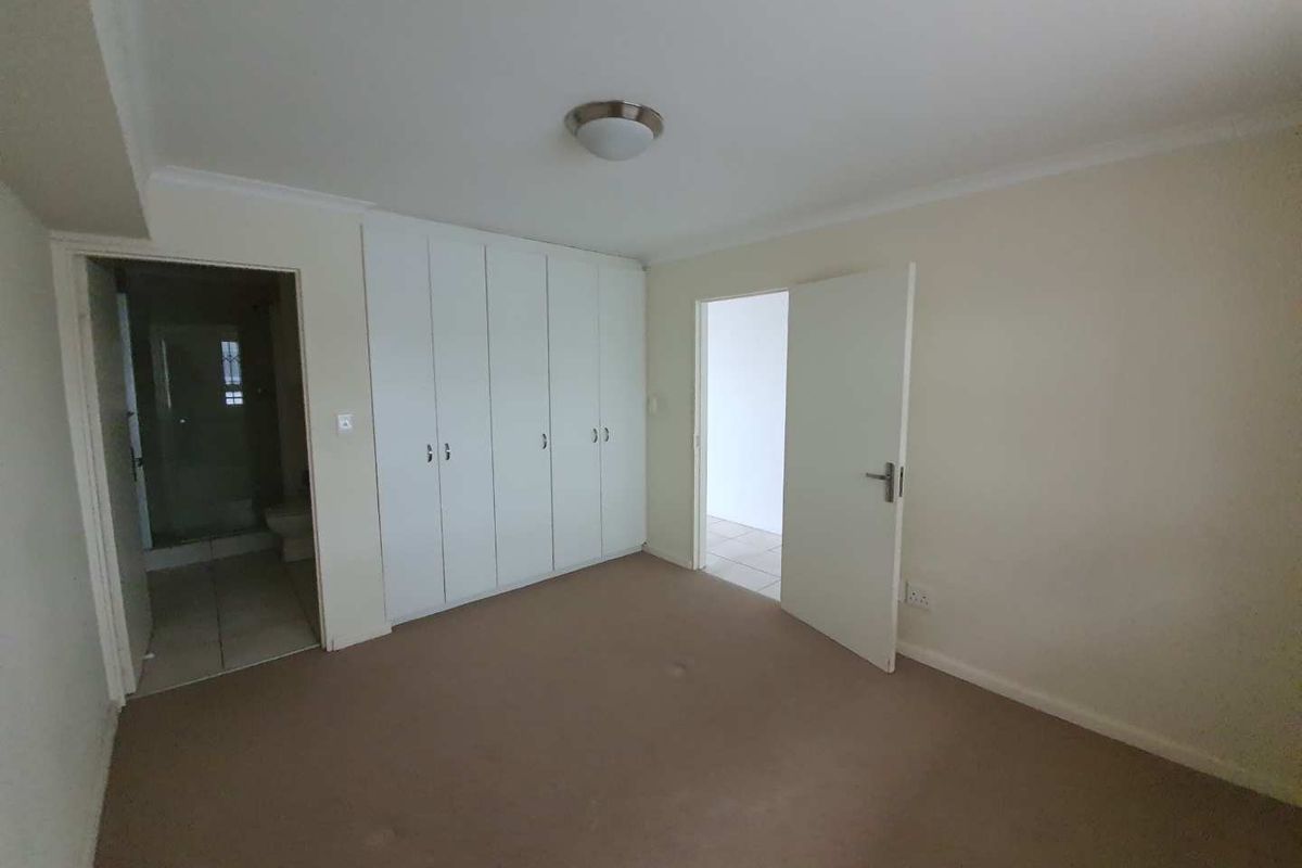 A spacious bedroom featuring built-in cupboards, neutral wall finishes, and direct access to an en-suite bathroom.